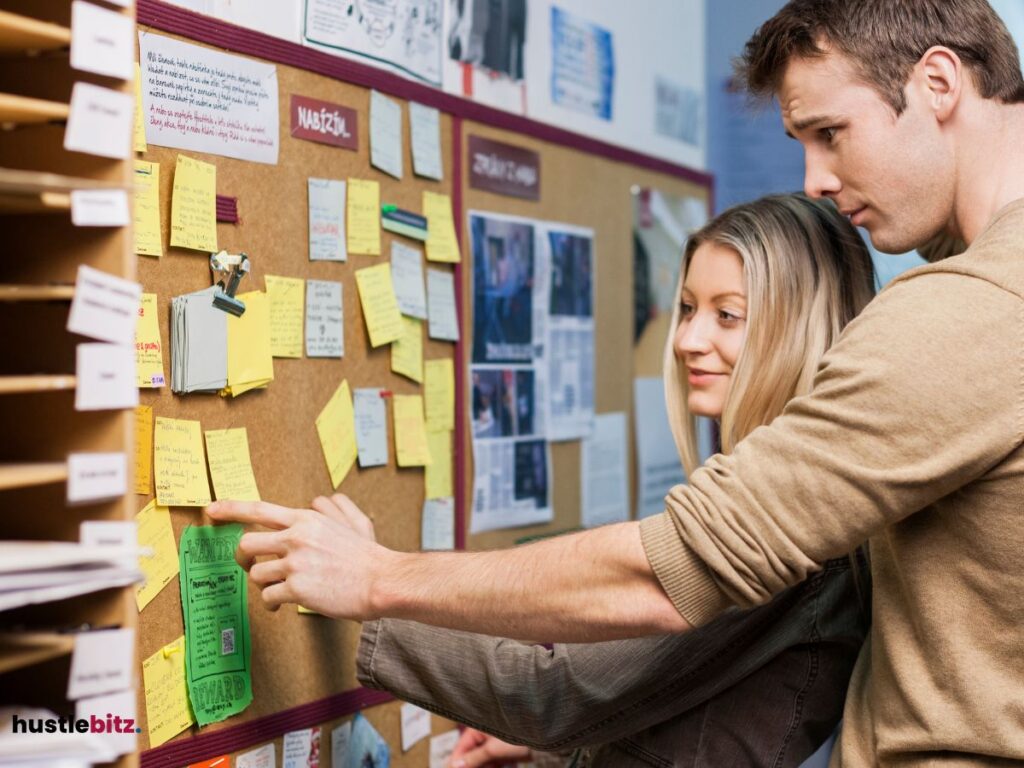 A man and woman pointing the sticky notes in the bulletin board