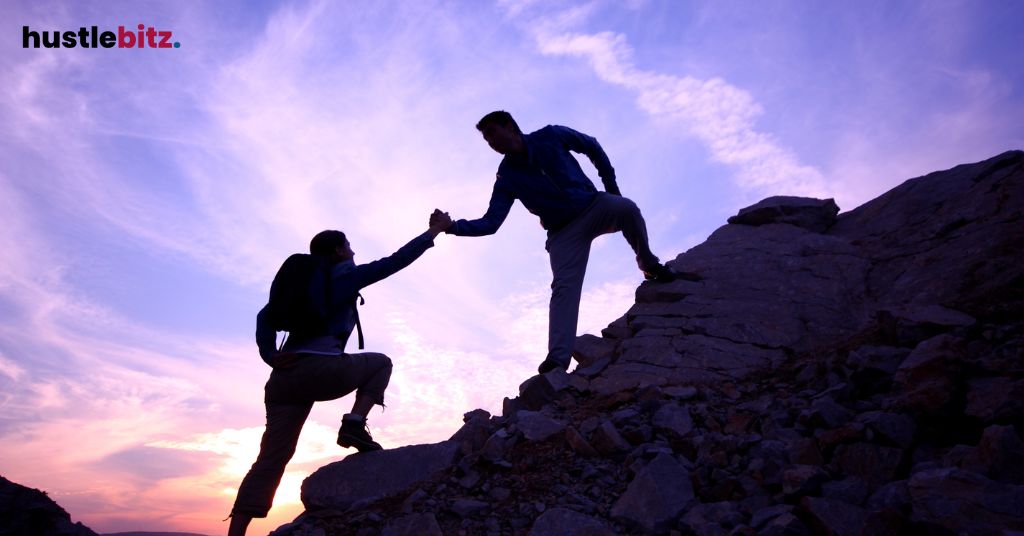 Two people helping each other climbing the mountain with a cloudy background