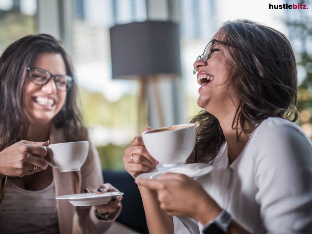 Two women laughing while enjoying coffee together in a cafe.