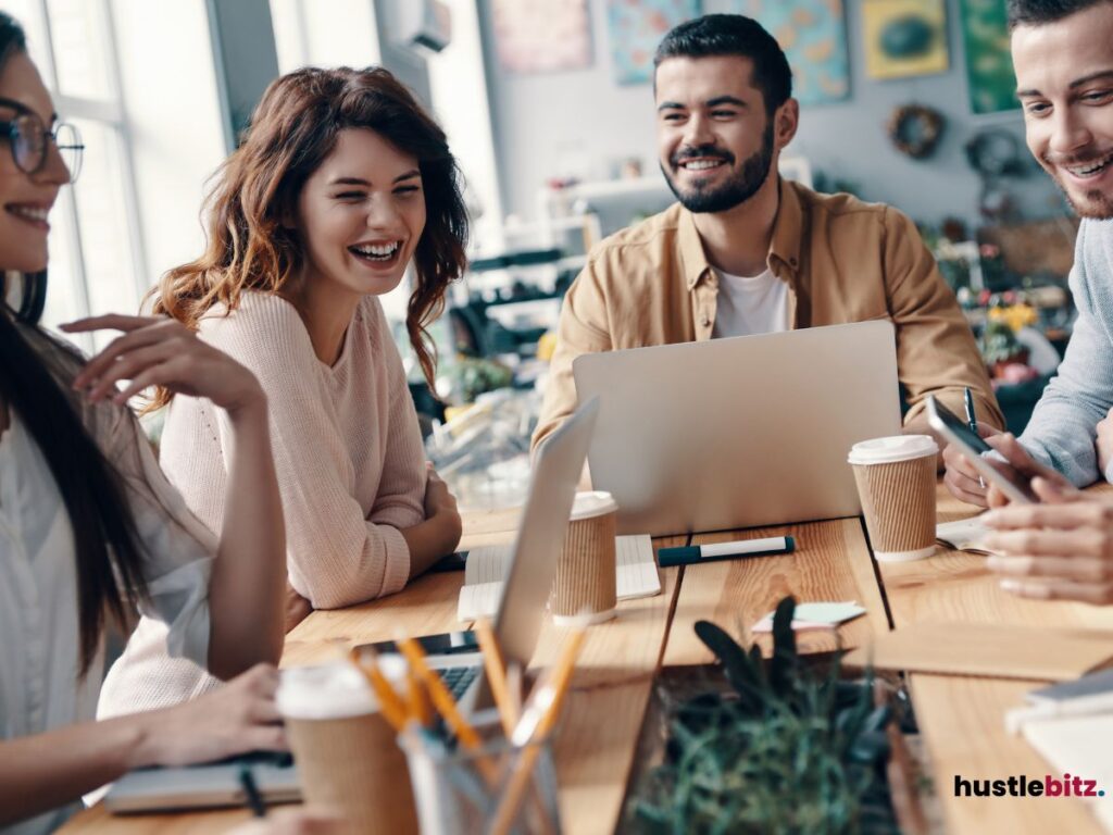 A group of young professionals sitting together, smiling and collaborating over laptops and coffee.