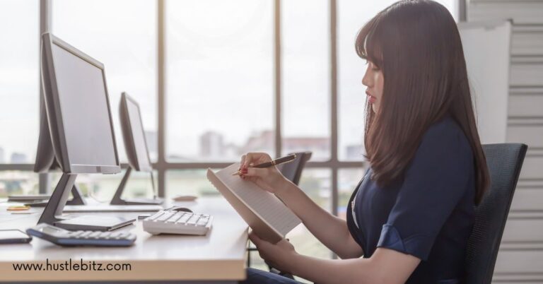 A woman doing writing inside the office and a table with monitor