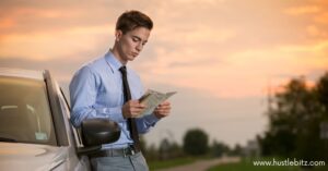 A man in a suit stands beside a car, reading a map during sunset.