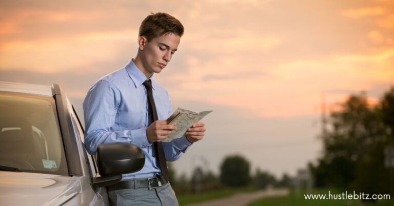 A man in a suit stands beside a car, reading a map during sunset.