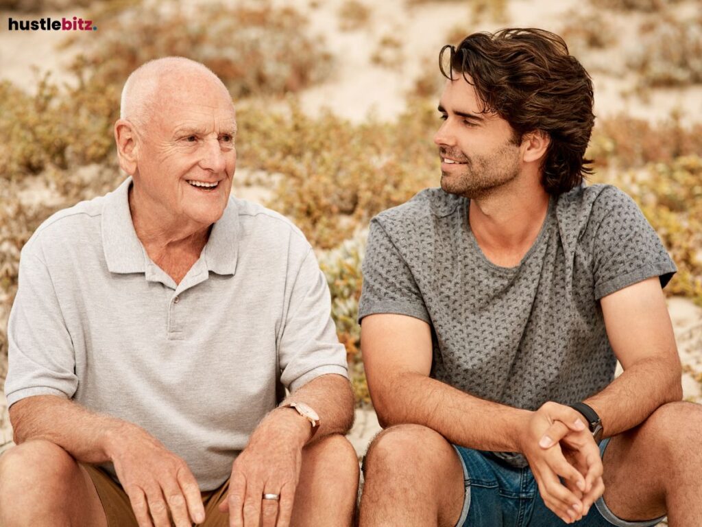 Elderly man and younger man sitting outdoors, engaged in conversation.