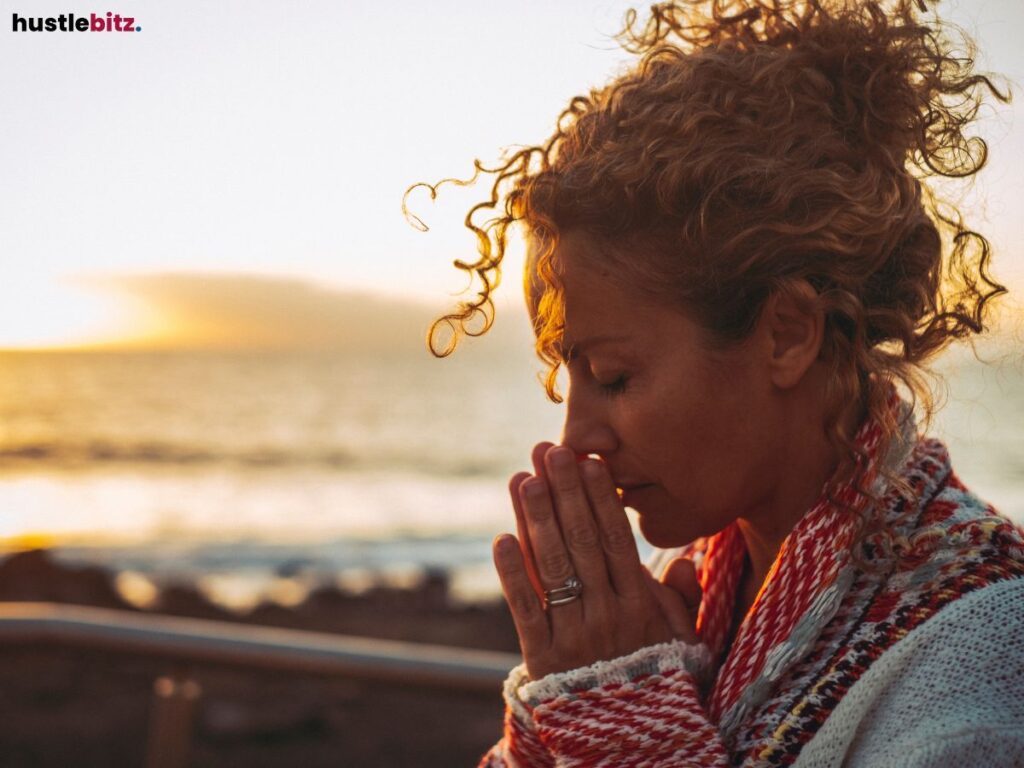 Woman with closed eyes, praying by the sea during sunset.