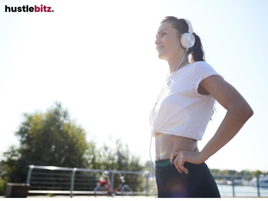 A smiling woman wearing headphones enjoys a sunny outdoor workout.