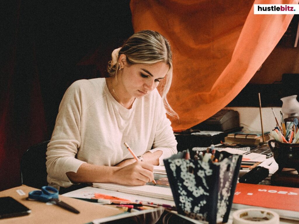A woman focused on drawing and organizing materials at her desk in a cozy, creative space.
