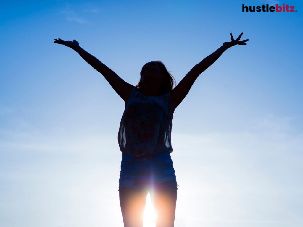 A silhouette of a woman with arms raised, basking in the sunlight.