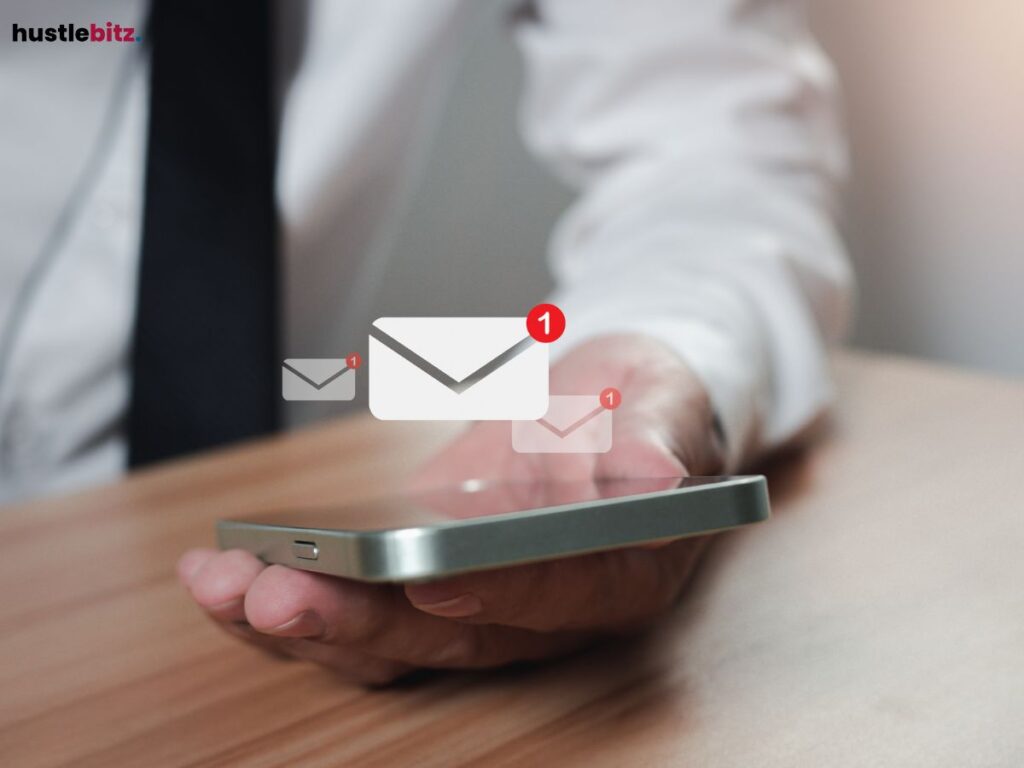 A hand holding a phone displaying incoming email notifications.