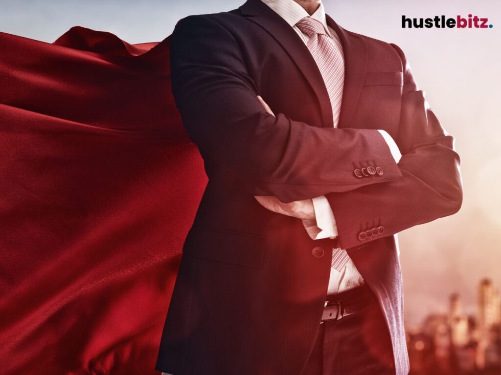 A man in a suit with a red superhero cape, standing with crossed arms.