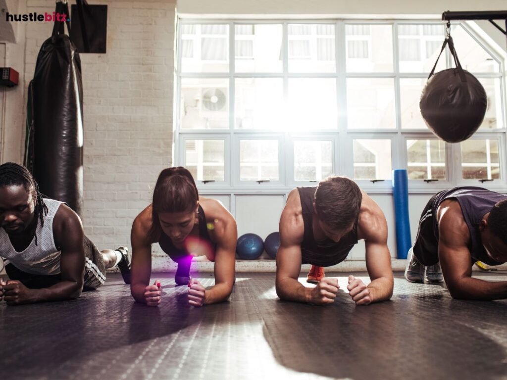 A group of people doing planks together in a gym setting, focused on their workout.