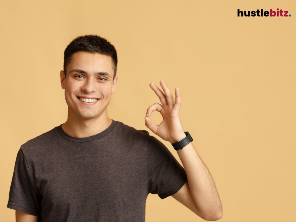 Smiling man giving an "OK" hand gesture against a beige background.