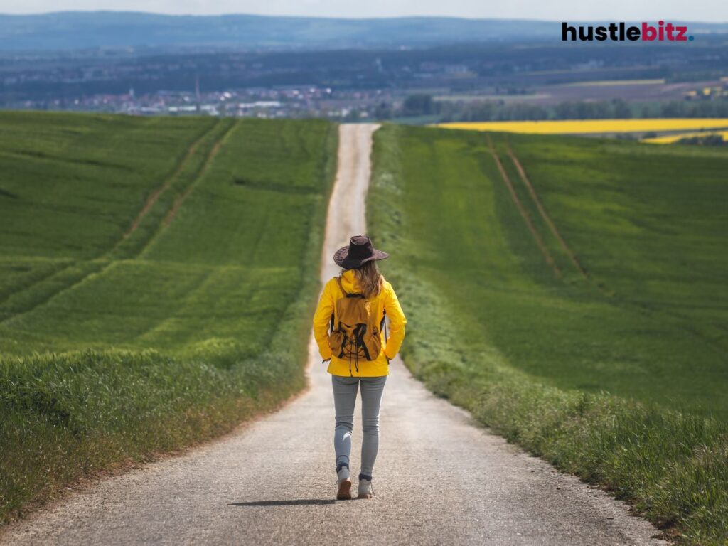 A woman wearing hat walking to the long road in front of her