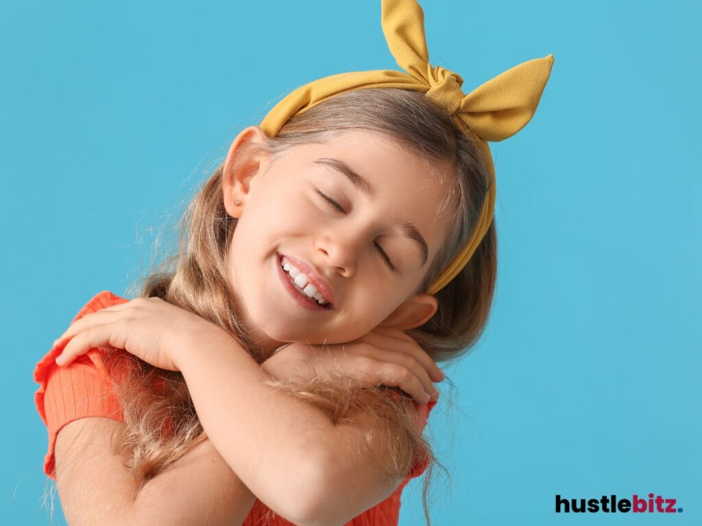 Smiling girl with closed eyes and a yellow bow, hugging herself.