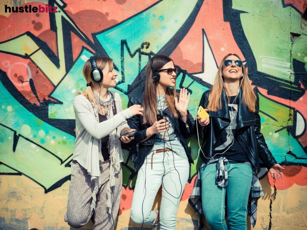 Three friends laughing and listening to music in front of colorful graffiti.