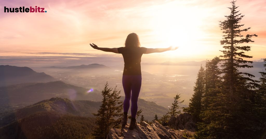 A woman raise her two hands facing the mountains and sunset