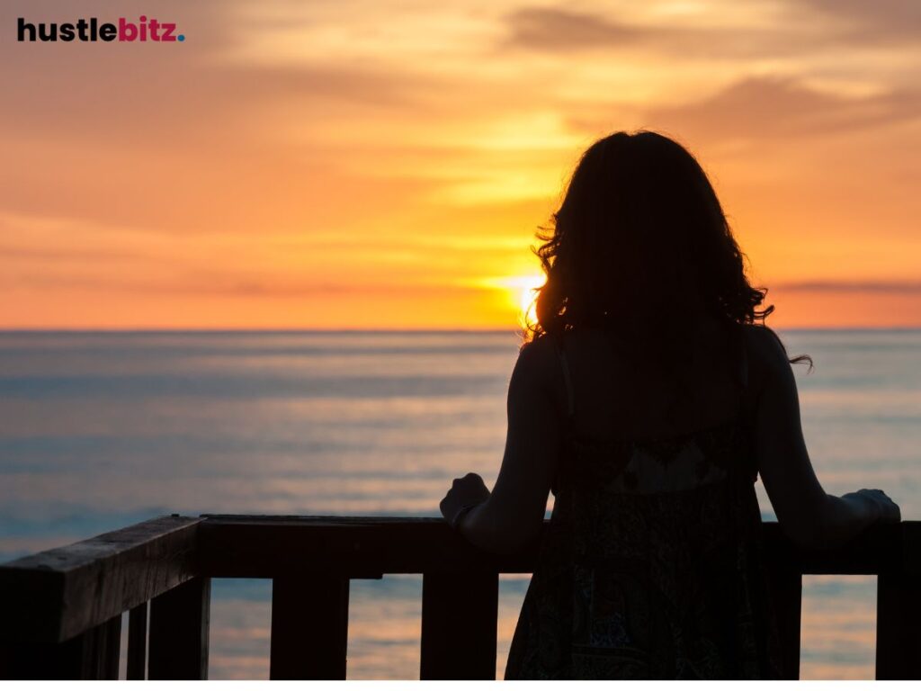 A person gazes at a sunset over the ocean from a wooden deck.