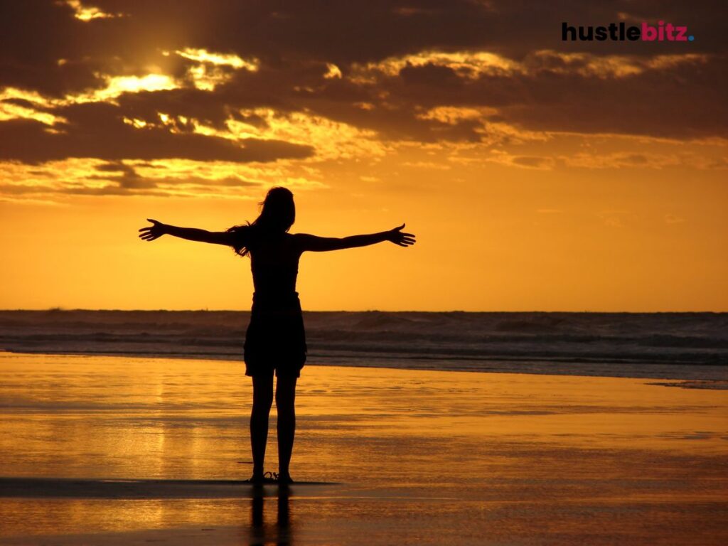 Person embracing the golden sunset at the beach with arms wide open.