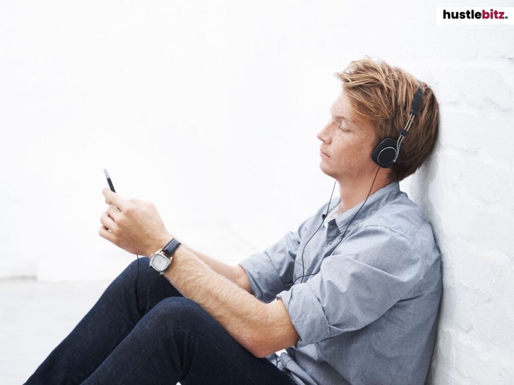 Young man sitting against a wall, wearing headphones