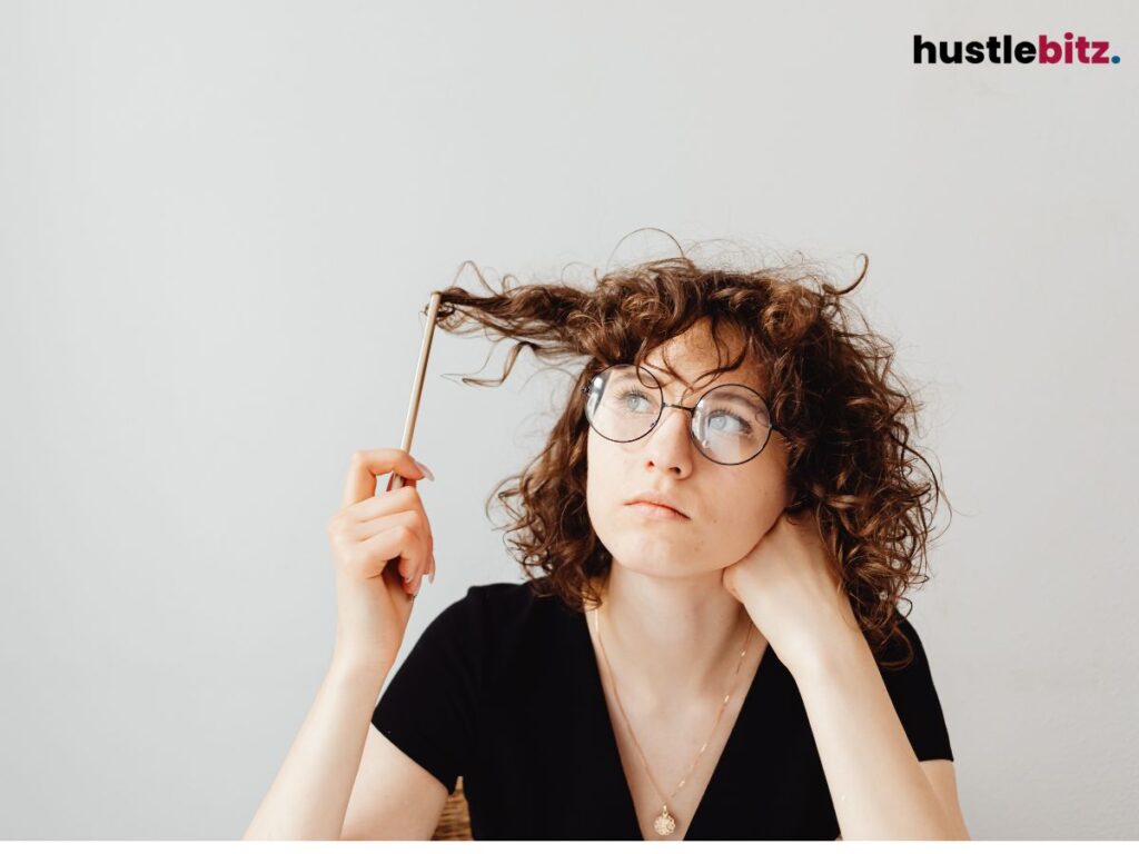 A woman in glasses playing with her hair while thinking.