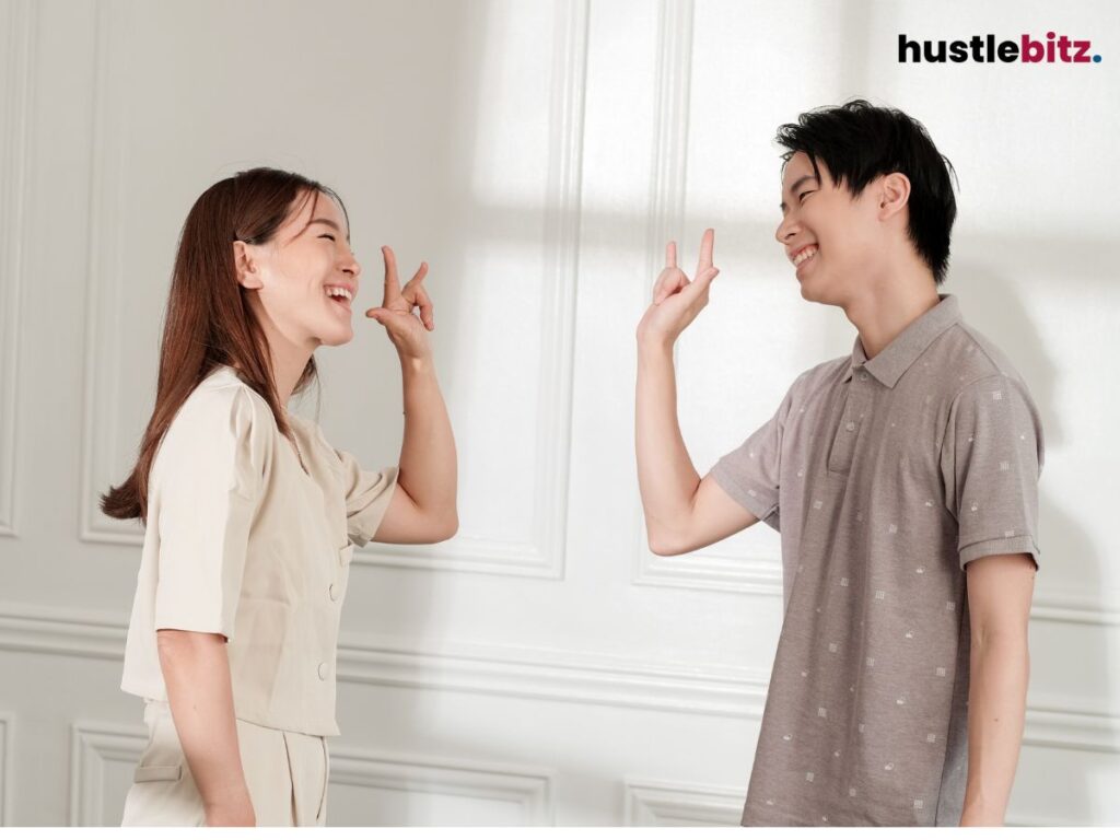 Two people laughing and gesturing a hand sign at each other.