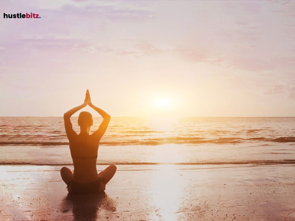 A person sitting in a lotus position facing the ocean at sunrise, practicing mindfulness.
