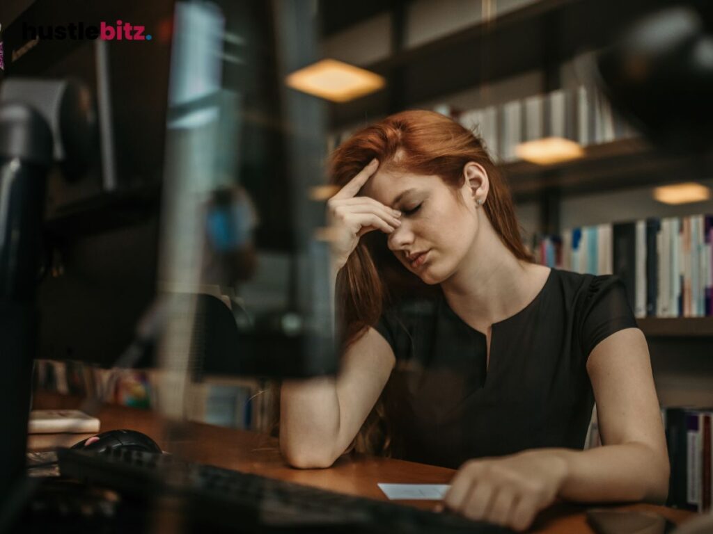 A stressed woman at her desk, head resting on her hand in frustration.