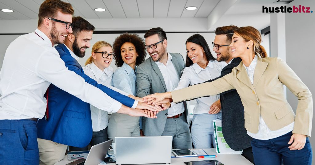 A group of people inside the office smiles and hold their hands together