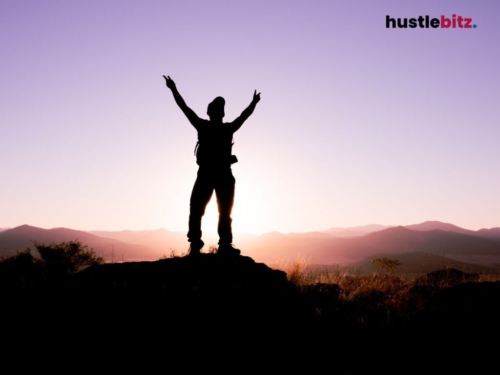 A silhouette raises arms in victory on a mountain at sunset, symbolizing triumph.