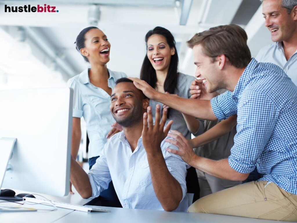 Team celebrating success around a computer in an office.