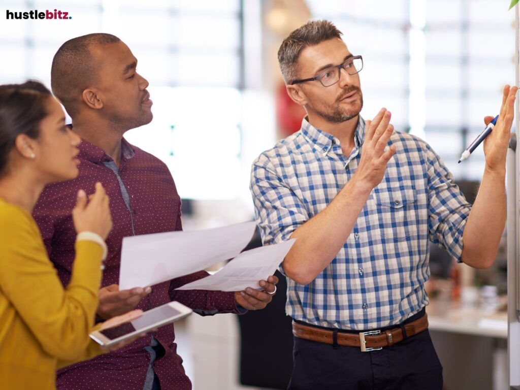 Group of three people in an office discussing ideas, one using a whiteboard.