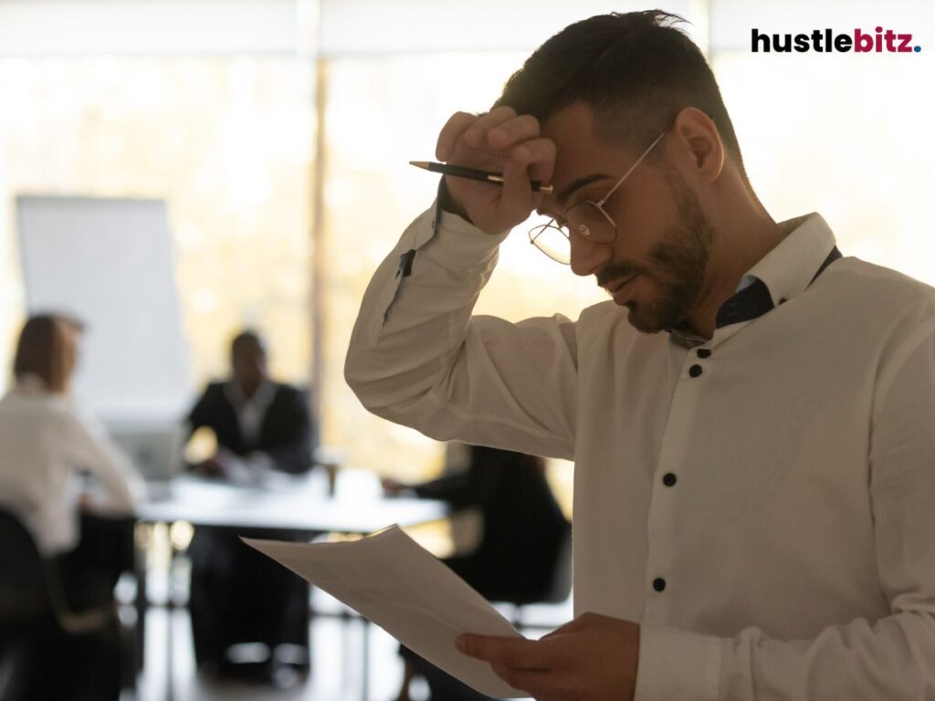 A man holds paper, rubbing his forehead, appearing stressed during a meeting.