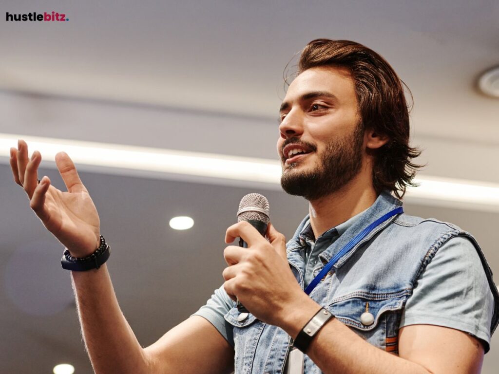 A young man speaking on stage with a microphone in hand.