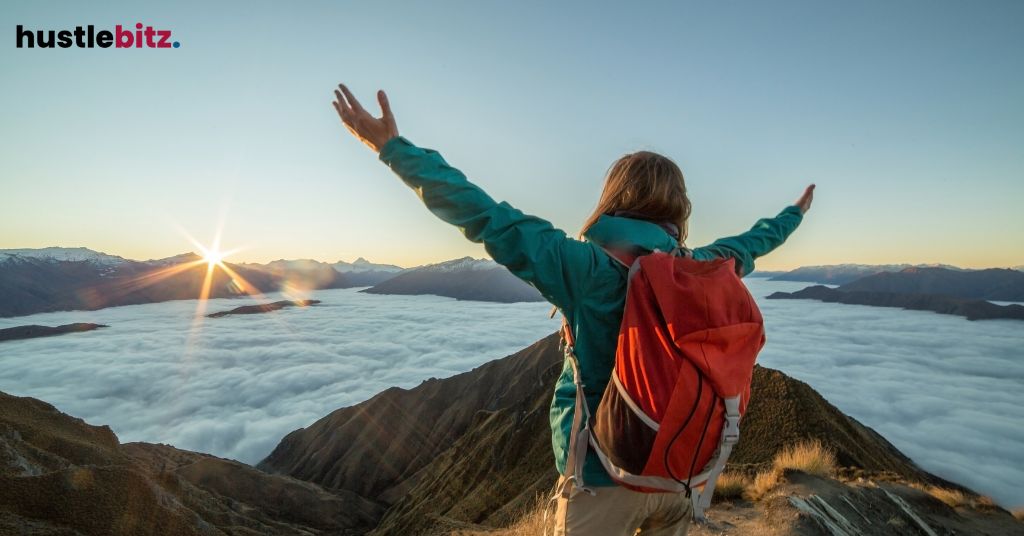 A person raise her two hands celebrating victory in front of mountains and clouds