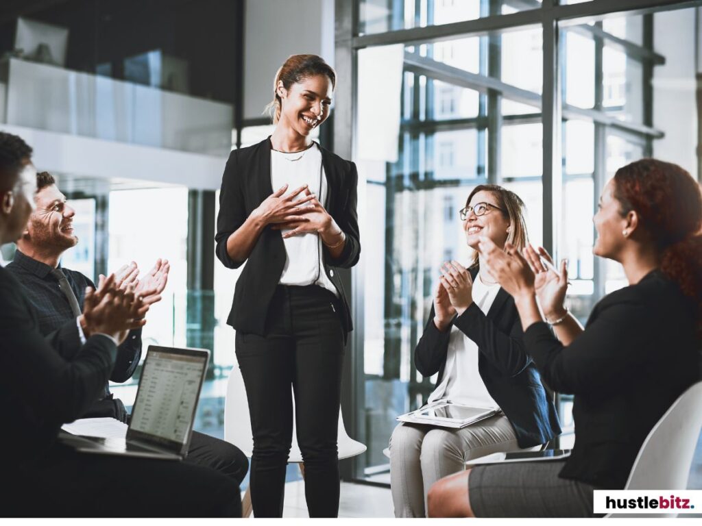 A group of people clapping to the woman standing