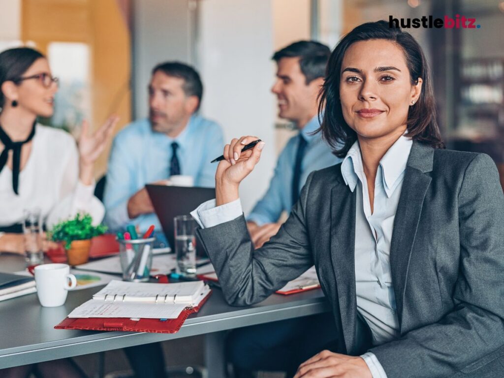 A confident businesswoman in a meeting, listening while holding a pen.