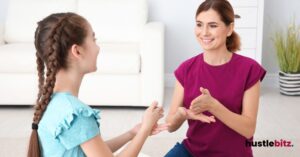 A woman teaching a young girl sign language in a bright room.