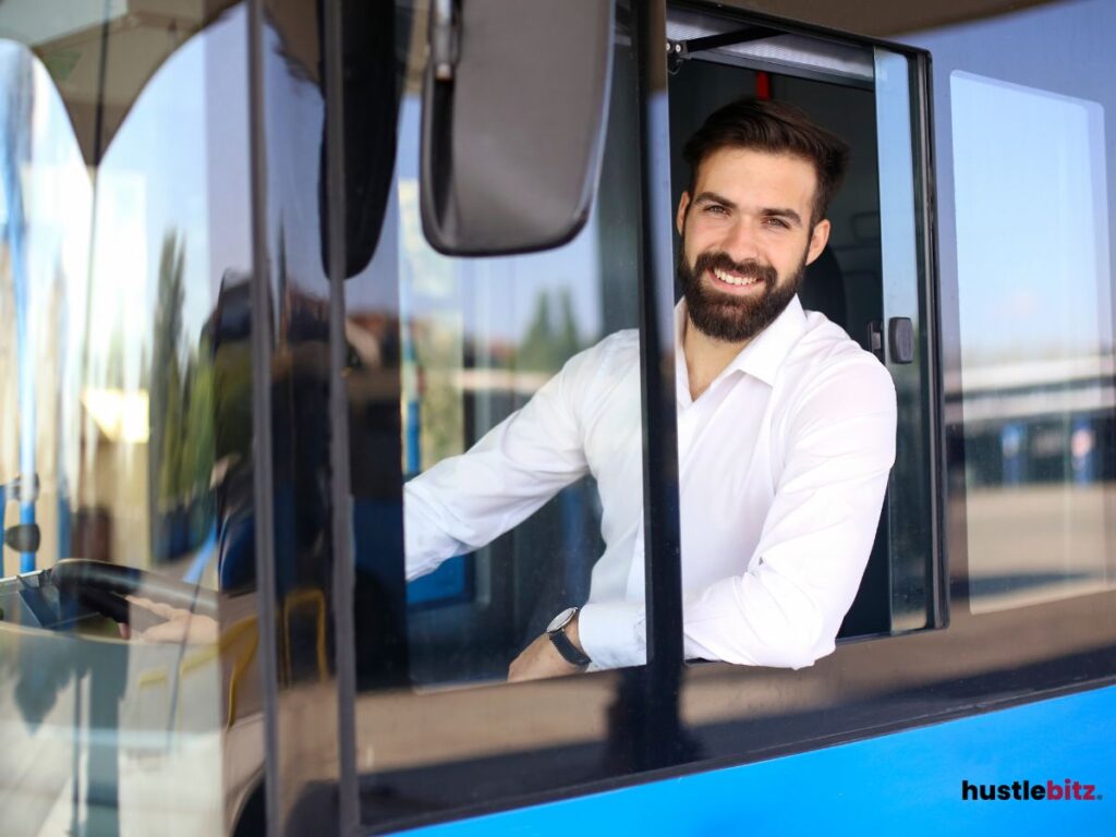 A man smiling in the driver's seat of the bus.