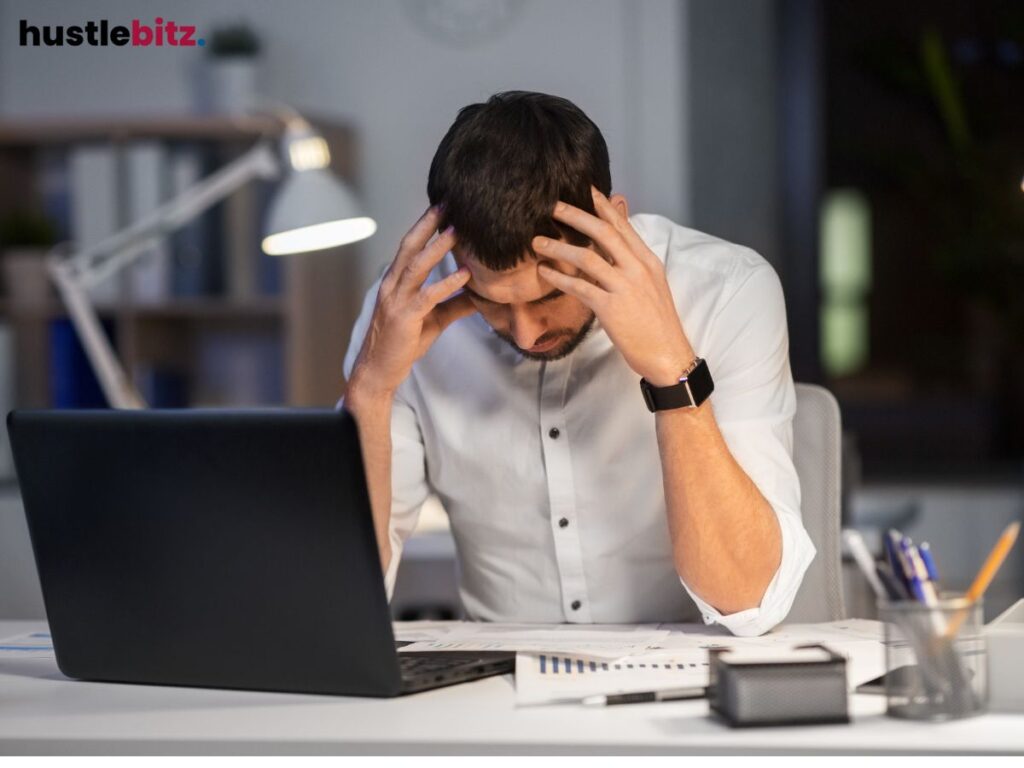 A man sits stressed at his desk, hands on head, deep in thought.