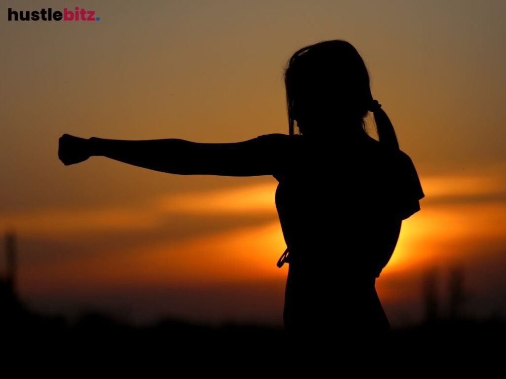 A silhouette of a woman practicing martial arts at sunset, symbolizing strength.