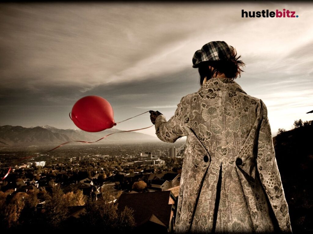 A person holds a red balloon, standing above a cityscape with mountains.