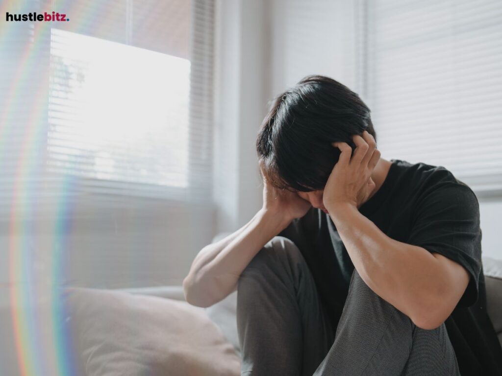 A man in the room sitting on the bed holding his head