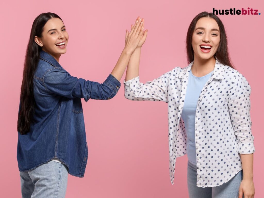 Two women smiling and giving each other a high five against a pink background.