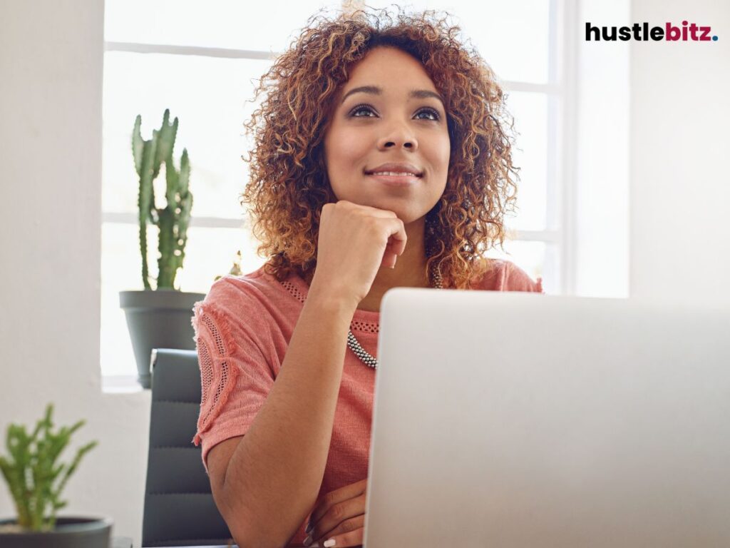 A woman at a desk looks upward, smiling thoughtfully, lost in her thoughts.