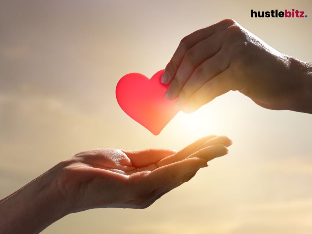A glowing red heart is passed between two hands in a gesture of care.
