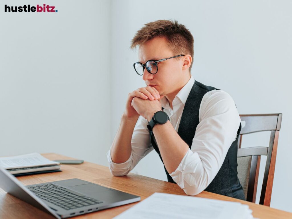 Focused man in glasses thinking while working on his laptop at a desk.