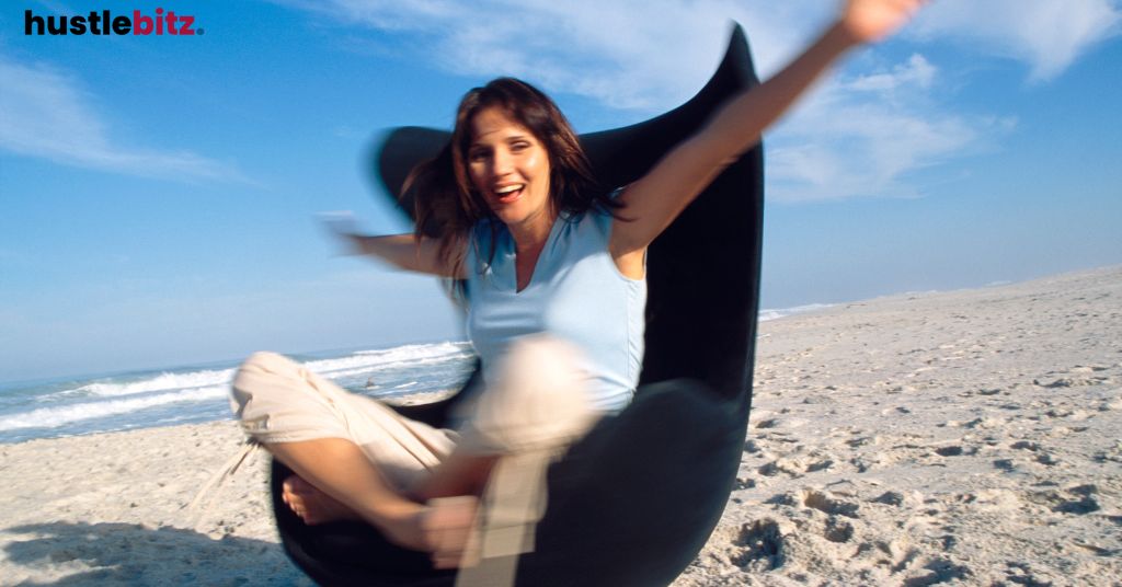 Woman spinning joyfully in a chair on a beach.