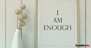 A framed quote saying "I Am Enough" next to a simple vase with spherical decor.