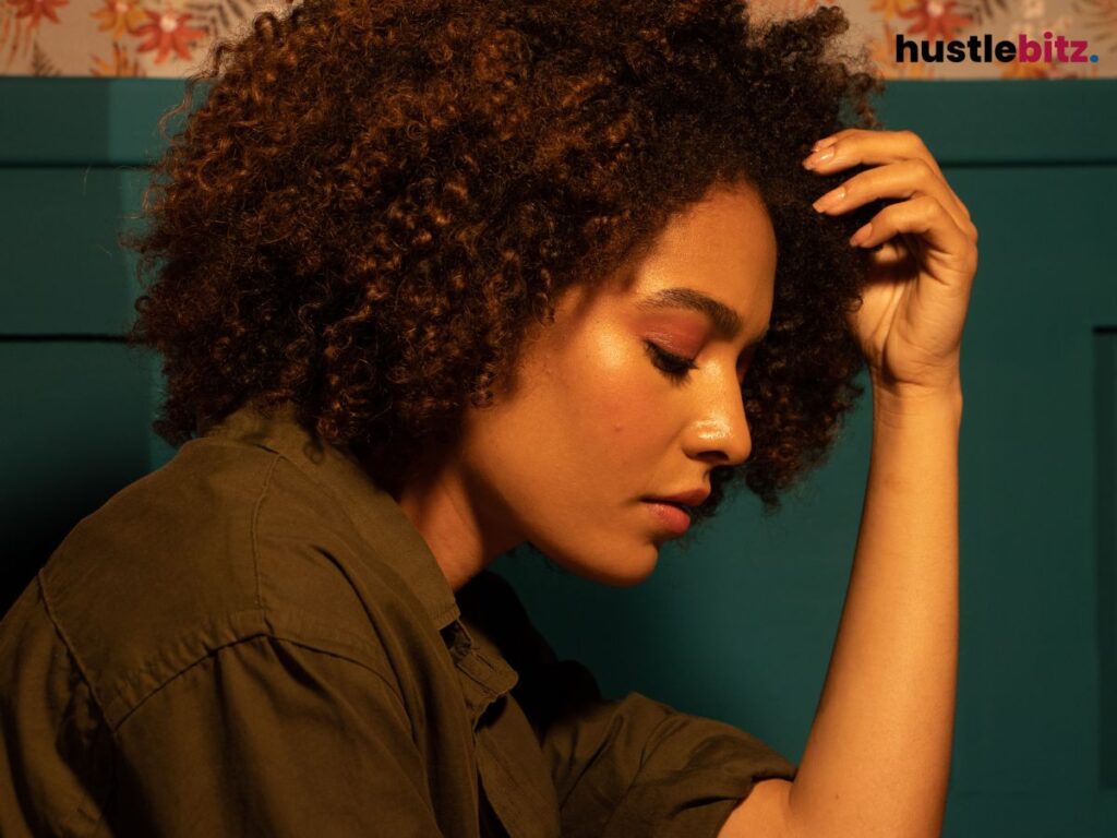 A woman rests her head in her hand, looking pensive in a dimly lit room.