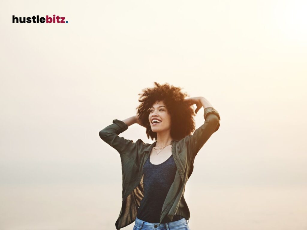 A woman smiles joyfully with open arms against a soft, glowing sky.


